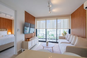 A modern hotel room with a bed, sofa, TV, and large windows offering a city view.