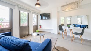 Una sala de estar moderna con un sofá azul, una pequeña mesa con una planta, un área de comedor con dos sillas y un espejo grande.