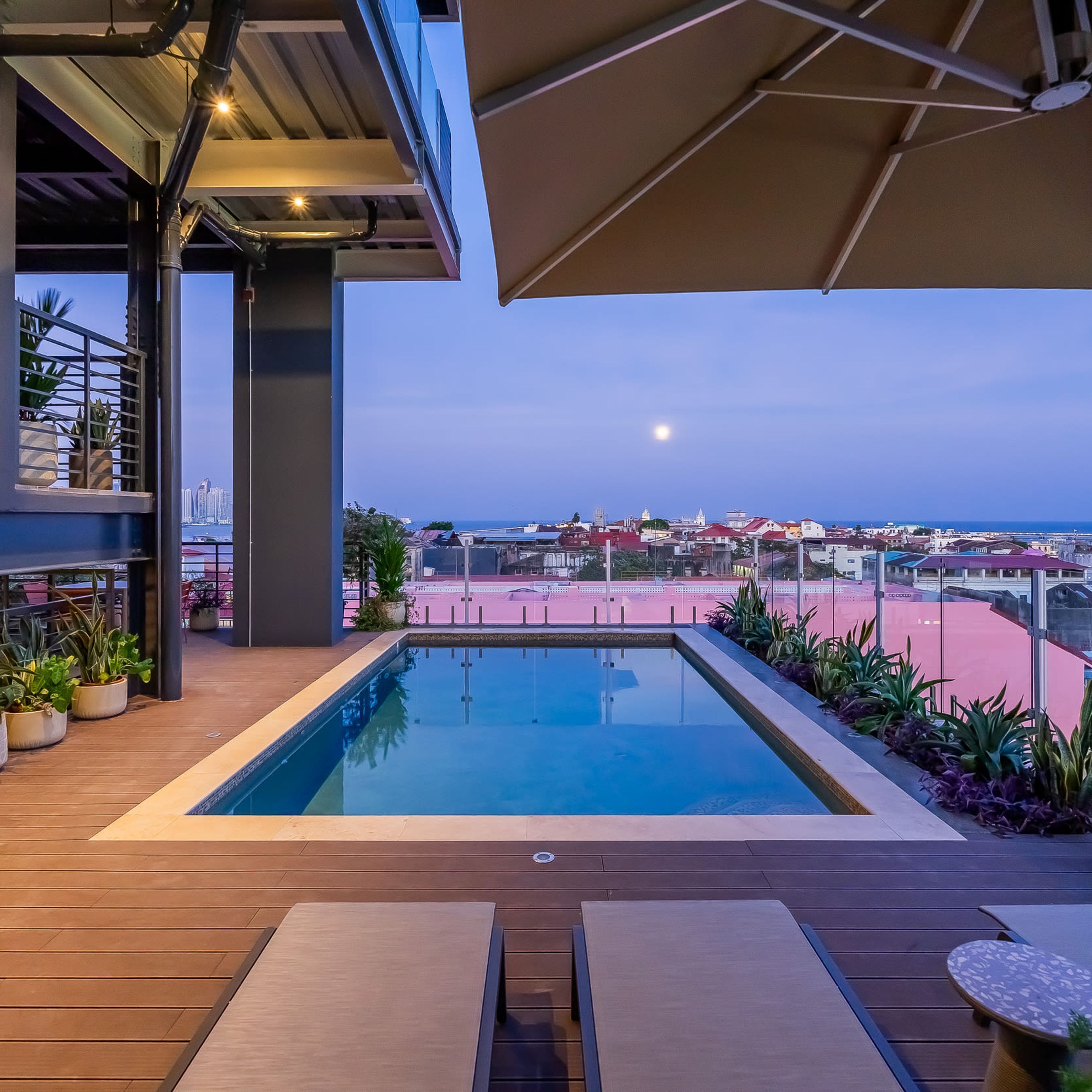 An outdoor swimming pool with a view of a cityscape and the sea at dusk.