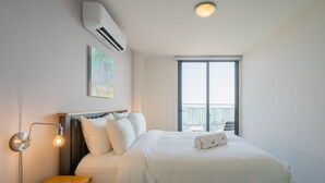 Camera d'albergo moderna con un letto, un comodino con una lampada, una finestra vista città e un condizionatore d'aria.