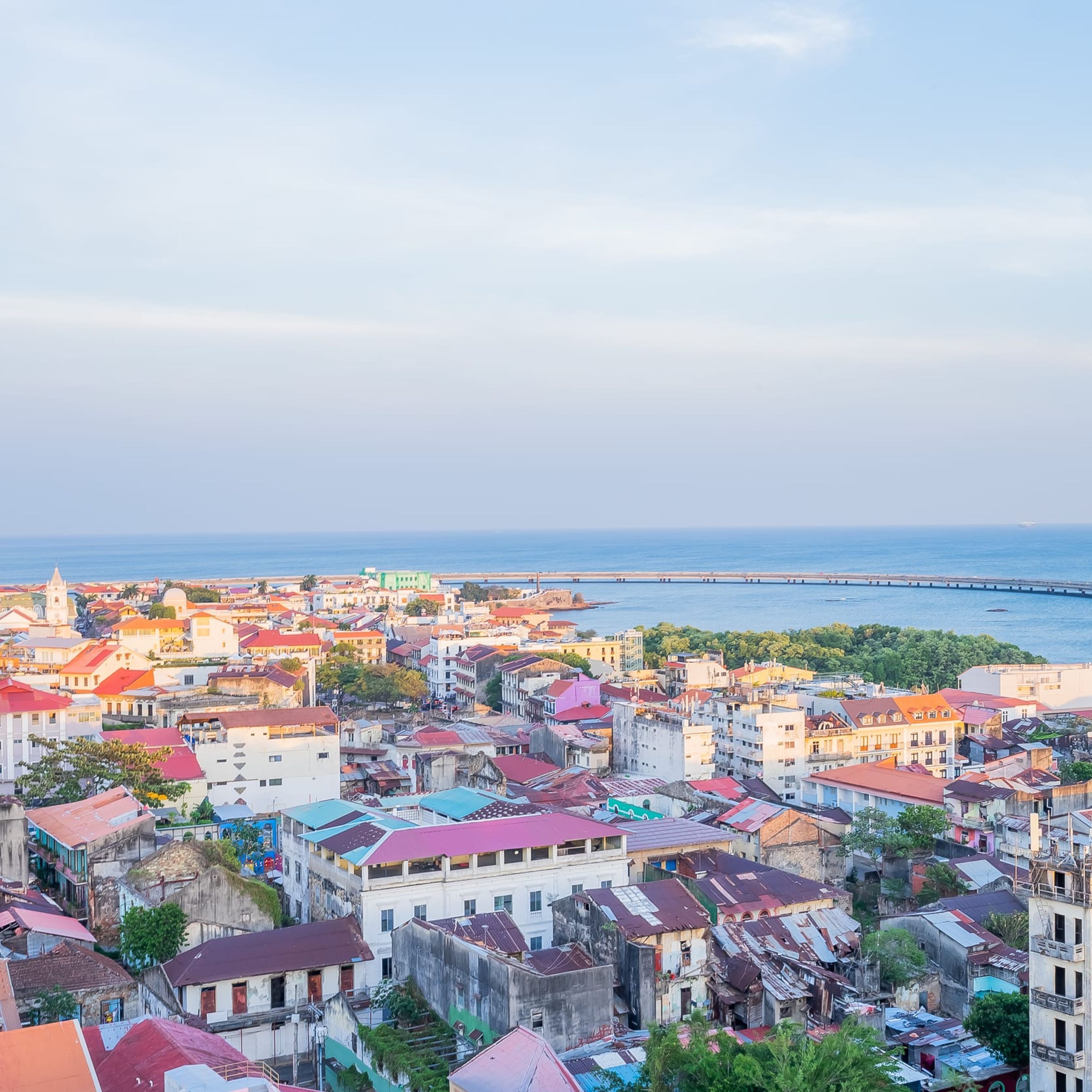 Un paisaje urbano costero con una mezcla de edificios coloridos, una imponente torre de iglesia y un muelle largo que se extiende al mar.