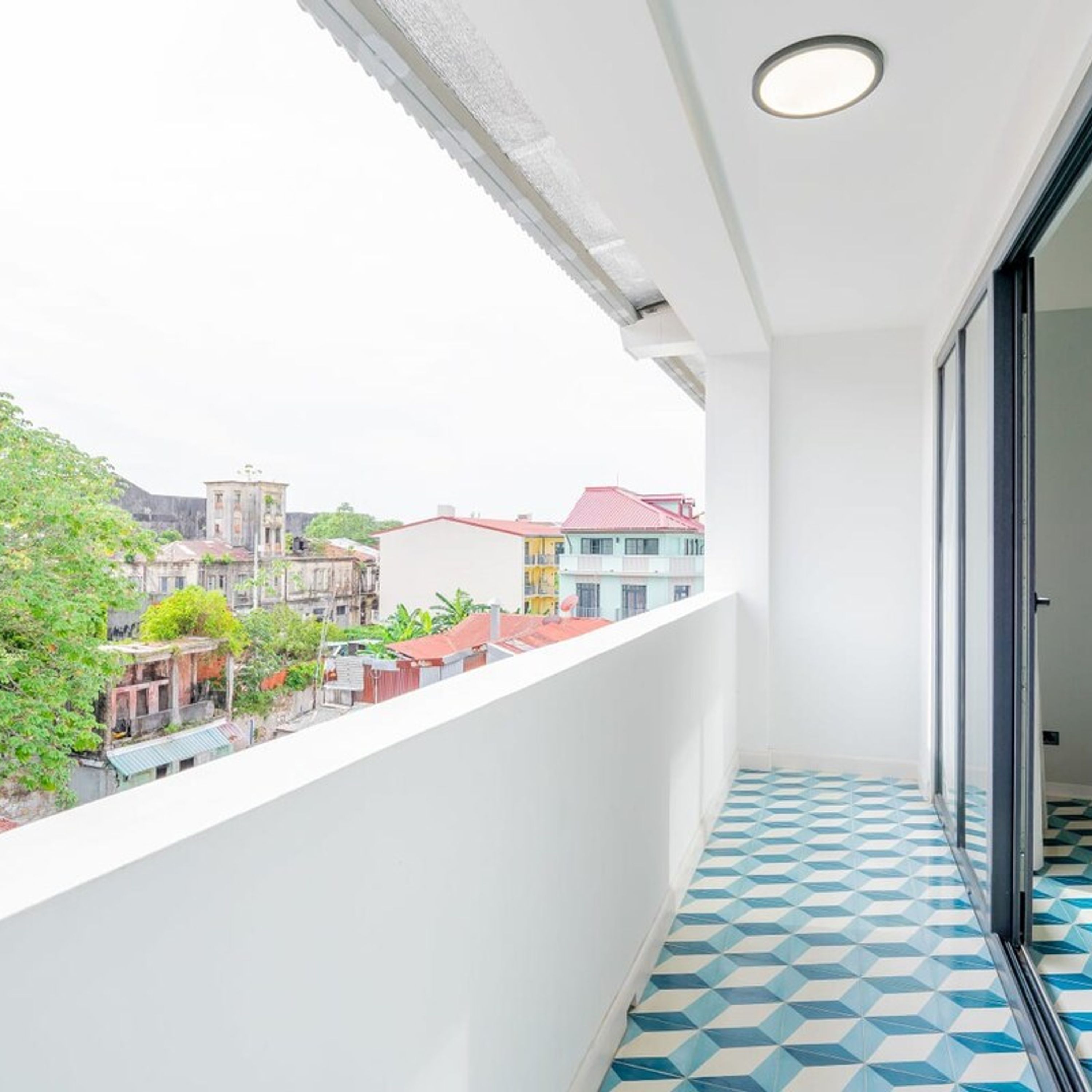 A balcony with a geometric patterned floor, a white wall, and a view of neighboring buildings.