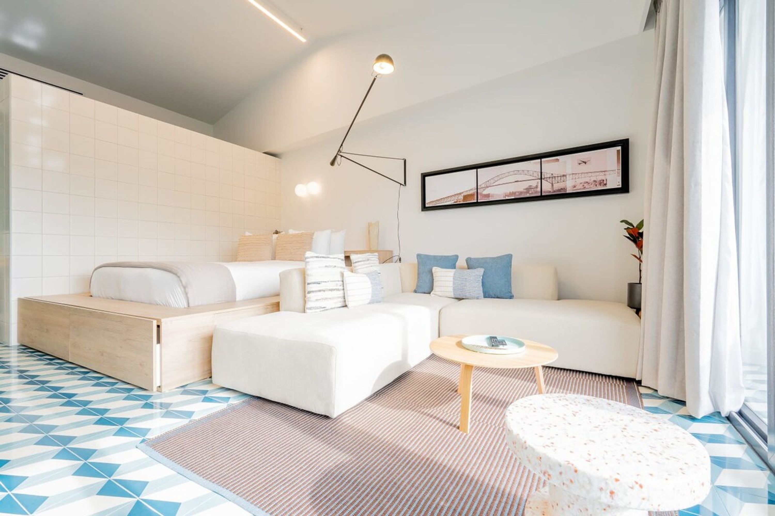 A modern hotel room with a sofa bed, a small round table, and a large window with curtains.