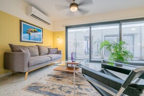 A modern living room with a gray sofa, a glass coffee table, and a large window with blinds. - w Homey 1BR in Casco Antiguo (Panama City)