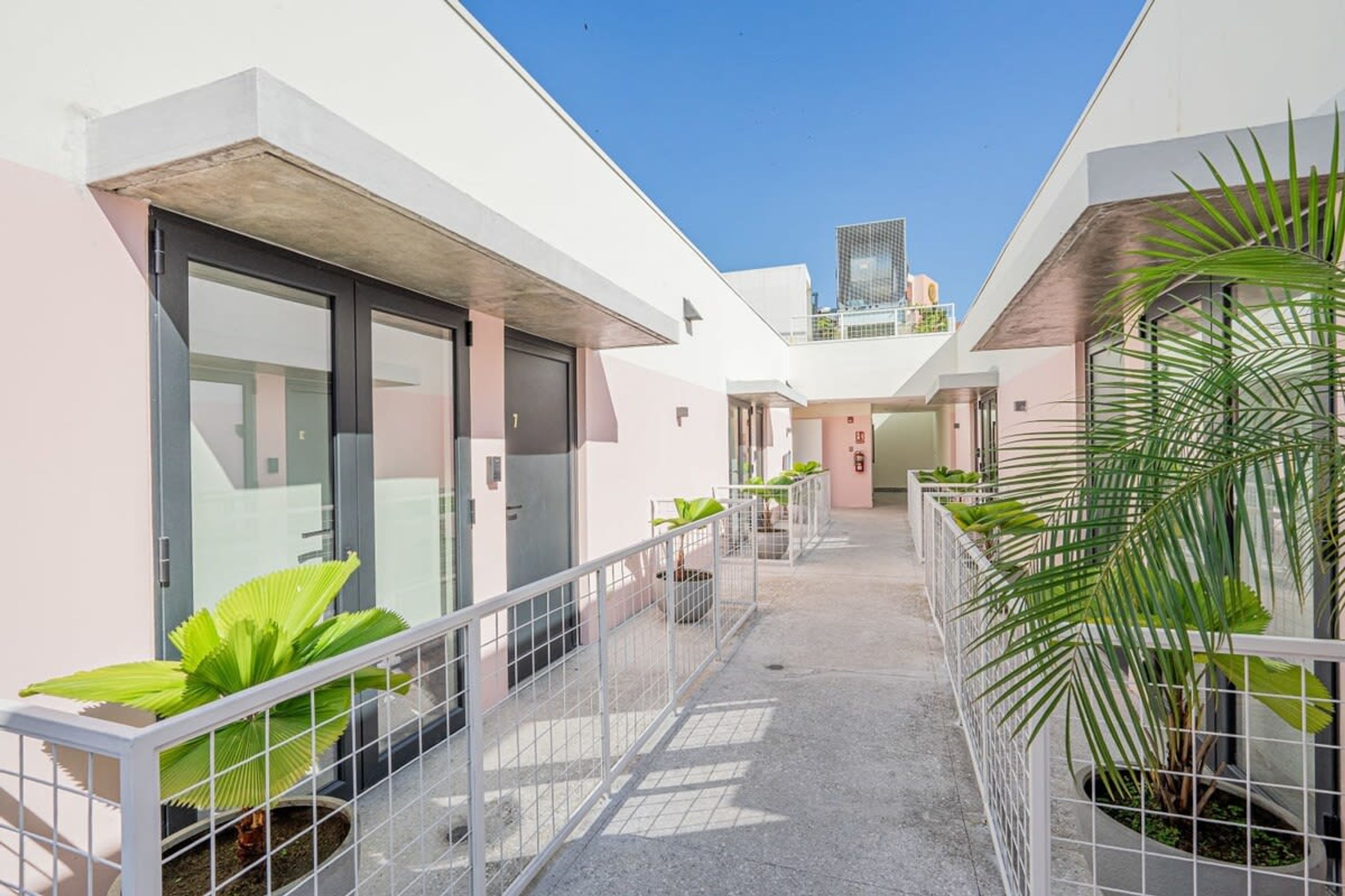 A modern building with a covered walkway, potted plants, and a clear blue sky.
