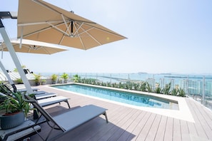 A rooftop pool area with lounge chairs and umbrellas, overlooking a cityscape and the sea. - Cozy 1BR With Balcony in Santa Ana (Panama City)