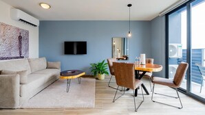 A modern living room with a sofa, a coffee table, a dining table with chairs, a TV mounted on the wall, and a large window with a view. - Cozy 1BR With Balcony in Santa Ana (Panama City)