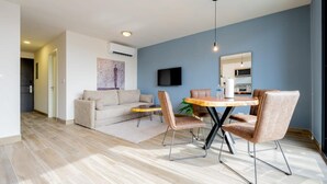 A modern living room with a sofa, a dining table with chairs, a TV mounted on the wall, and a kitchen area in the background. - Cozy 1BR With Balcony in Santa Ana (Panama City)