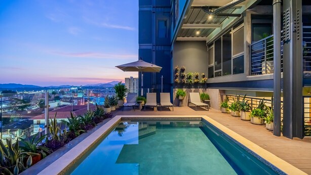 A rooftop pool with lounge chairs and potted plants, overlooking a cityscape at dusk. - Cozy 1BR With Balcony in Santa Ana (Panama City)