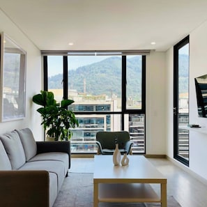 A modern living room with a sofa, a coffee table, and a plant. - w Amazing 1BR With Balcony in Chico (Bogotá)
