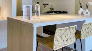 A modern kitchen with white cabinetry, a central island, and two wicker chairs. - w Amazing 1BR With Balcony in Chico (Bogotá)