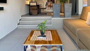 Un salon moderne avec un canapé, une table basse et deux plantes en pot. Un escalier mène à une autre pièce, et un téléviseur à écran plat est fixé au mur.