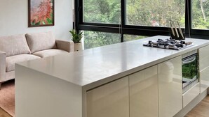 A modern kitchen with a large island, a built-in oven, and a window with a view of trees and buildings. - w Captivating 1BR in El Poblado (Medellín)