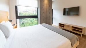 A modern hotel room with a large bed, a TV mounted on the wall, and a window with a city view. - w Captivating 1BR in El Poblado (Medellín)