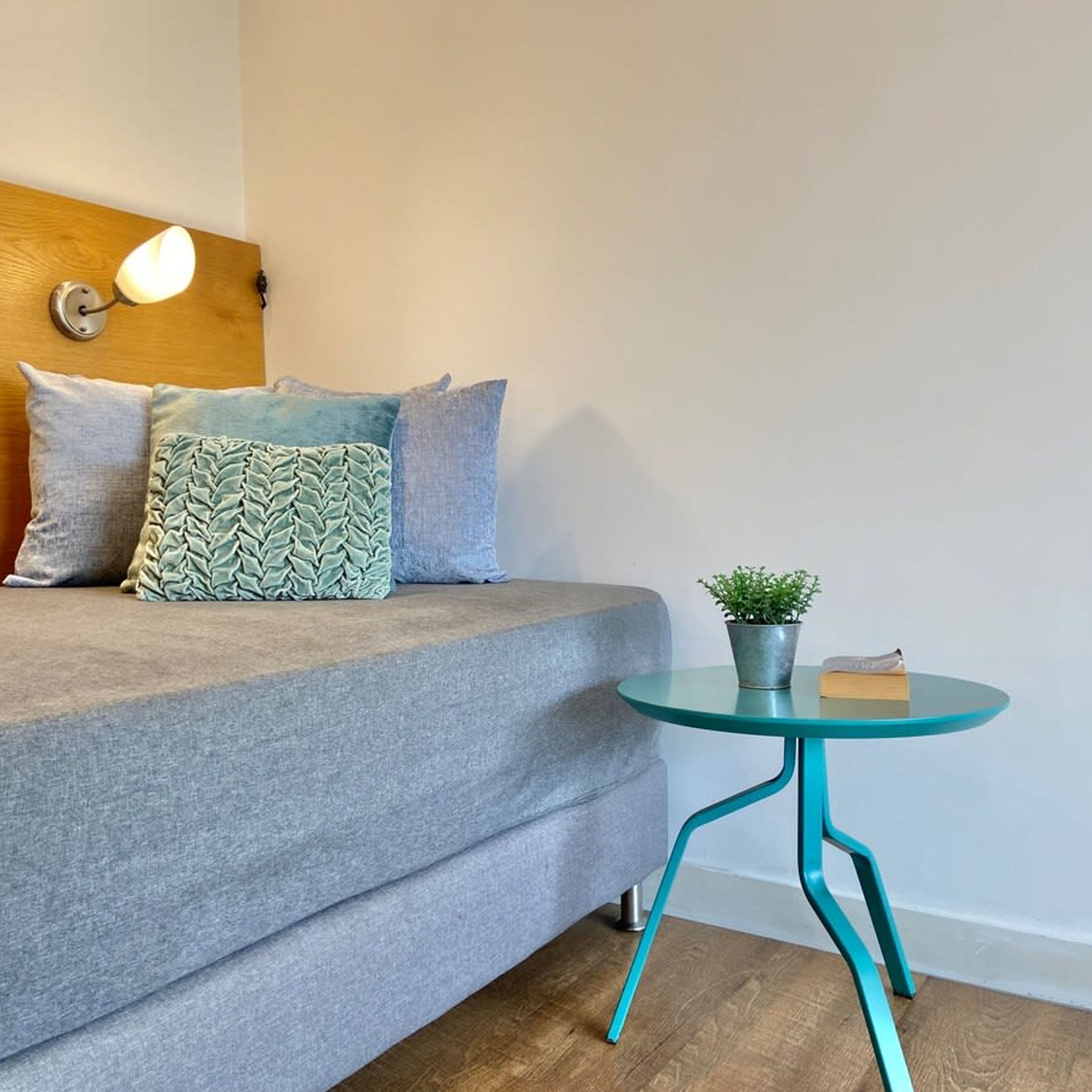 A modern bedroom with a grey sofa, a wooden headboard, and a small teal table with a plant.