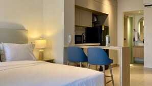 Et moderne hotelværelse med en stor seng, et skrivebord med to stole, et tekøkken og et badeværelse, der kan ses gennem en åben dør.
