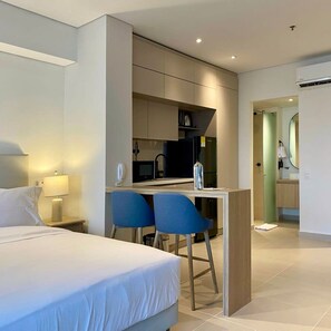 A modern hotel room with a bed, a desk, and a kitchenette.
