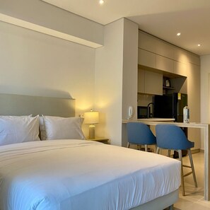 A modern hotel room with a large bed, a desk, and a kitchenette.