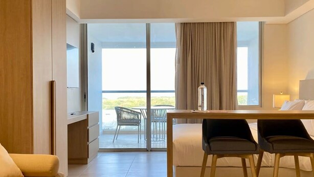 Et moderne hotelværelse med seng, skrivebord, to stole, sofa og balkon med udsigt.