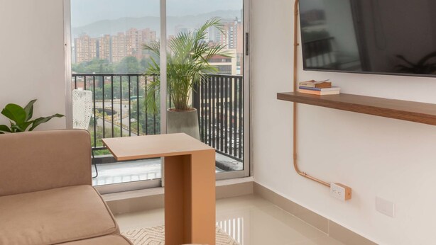 A modern apartment with a sliding glass door leading to a balcony, a flat-screen TV mounted on the wall, and a small table with books. - w Spectacular 1BR With Terrace at Poblado (Medellín)