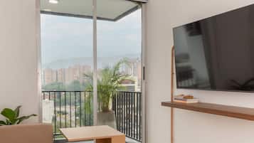 Um apartamento moderno com uma porta de vidro deslizante que dá para uma varanda, uma televisão de tela plana na parede e uma pequena mesa com livros.