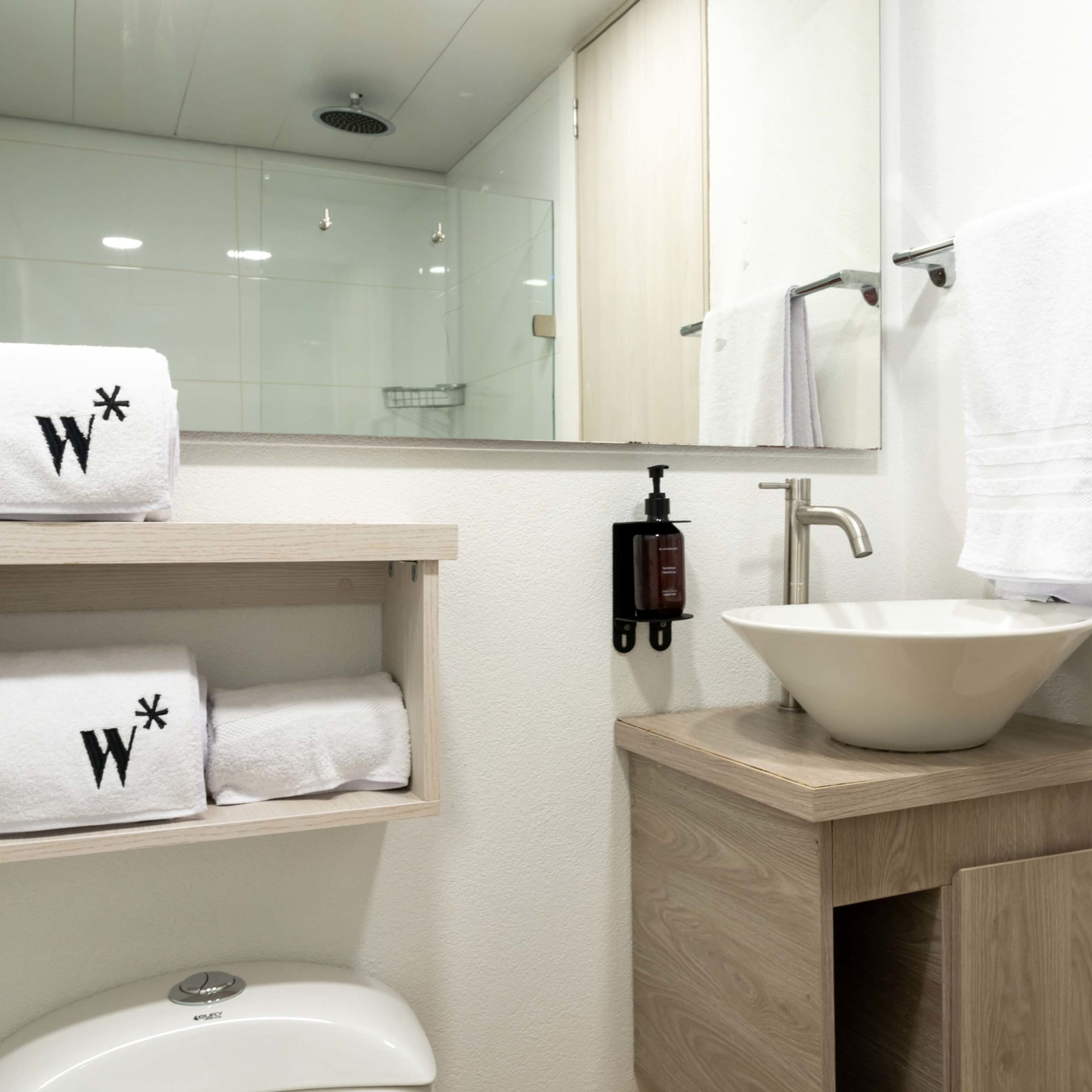 Une salle de bain avec un lavabo blanc, un miroir et des étagères où sont rangées des serviettes.