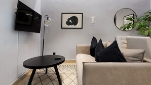 A modern living room with a flat-screen TV, a framed abstract artwork, a round mirror, a beige sofa with black cushions, and a small black table with a remote control. - w Cozy 1BR in Polanco (Mexico City)