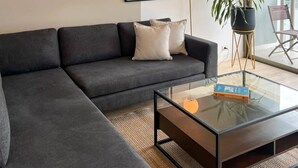 Ein modernes Wohnzimmer mit einem dunkelgrauen Sofa, einem Glastisch und einem Stadtbild an der Wand.