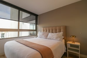 A bedroom with a large bed, a window, and a bedside table with a lamp. - Amazing 2BR in Miraflores (Lima)