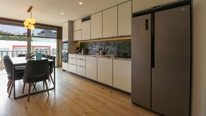 Eine moderne Küche mit Essbereich, ausgestattet mit einem großen Kühlschrank, Schränken und einer Pendelleuchte.