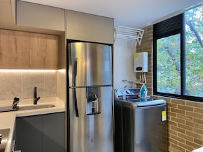 A modern kitchen with stainless steel appliances, a built-in oven, a water heater, and a window with a view of trees. - w Wonderful 2BR With Modern Deco in Laureles (Medellín)
