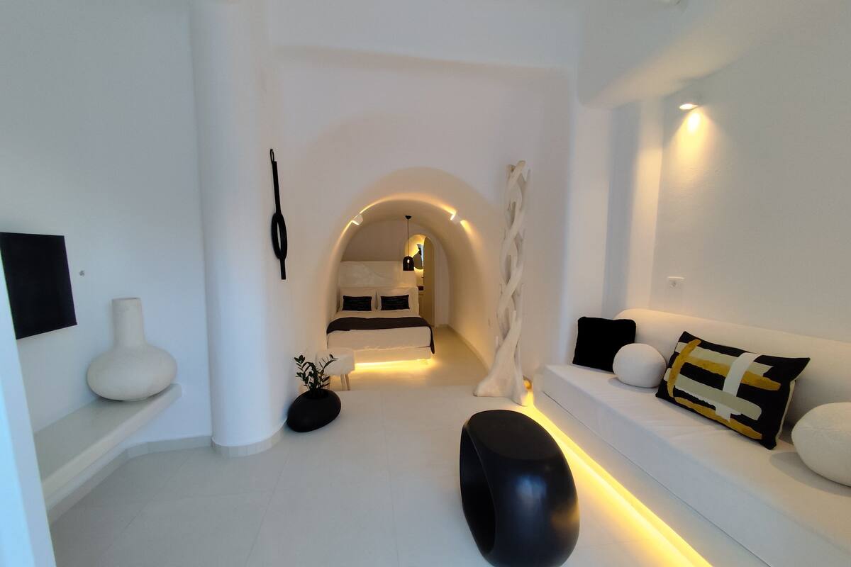 A modern, minimalist living room with a sofa, a black ottoman, and a white vase.