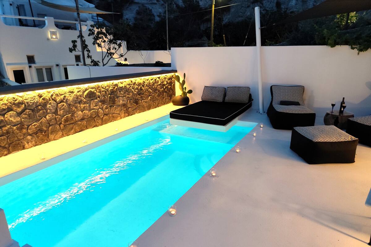 A modern outdoor pool area with a stone wall, lounge seating, and a small table with candles.