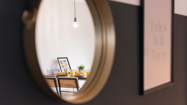 A dining area with a table set for two, a framed picture on the wall, and a hanging light fixture.