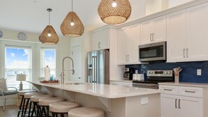 A modern kitchen with white cabinets, a large island with stools, a built-in oven, and a microwave. - Sea Cliff K66 Sunset on the Cape (Port St. Joe)