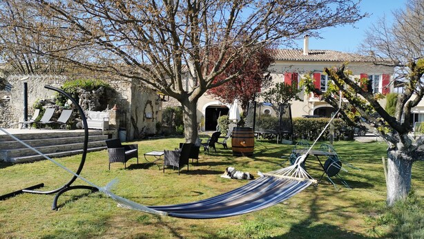 A grassy outdoor area with a hammock, outdoor seating, and a stone building in the background.