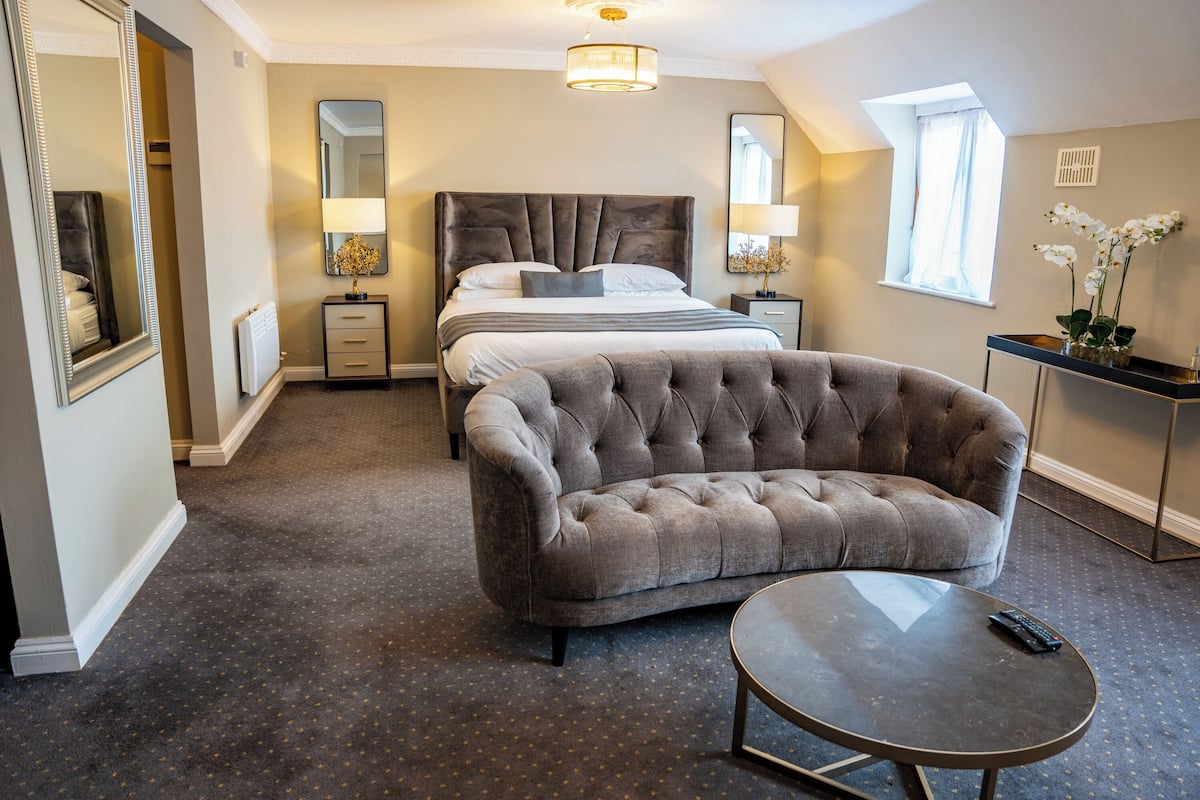 A bedroom with a large bed, a tufted armchair, a round coffee table, and a nightstand with lamps.