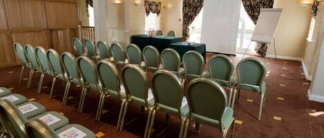 Un salón de conferencias con filas de sillas, una mesa y una pizarra.