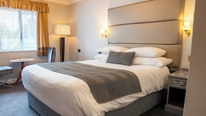 A neatly made bed with a grey blanket, a bedside table with a lamp, and a chair in a hotel room.