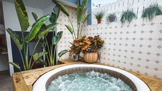 A hot tub in a wooden tub surrounded by potted plants and a tiled wall. - Boho Beach Villa - patio w/ bbq. 2 min to the beach, 15 to Lisbon (Trafaria)