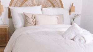 A neatly made bed with a wooden frame, white bedding, and a woven headboard. - Boho Beach Villa - patio w/ bbq. 2 min to the beach, 15 to Lisbon (Trafaria)