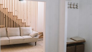 A modern living room with a sofa, a hanging light fixture, and a staircase in the background. - Boho Beach Villa - patio w/ bbq. 2 min to the beach, 15 to Lisbon (Trafaria)