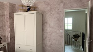 Un dormitorio con un amplio armario blanco, una mesita de noche con lámpara y vistas a una escalera que lleva a un balcón.