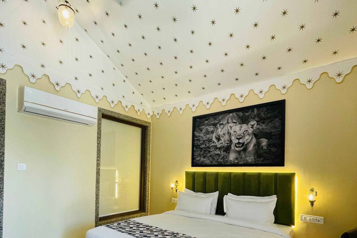 A bedroom with a bed, a wall-mounted air conditioner, a framed picture, and a ceiling with star patterns.