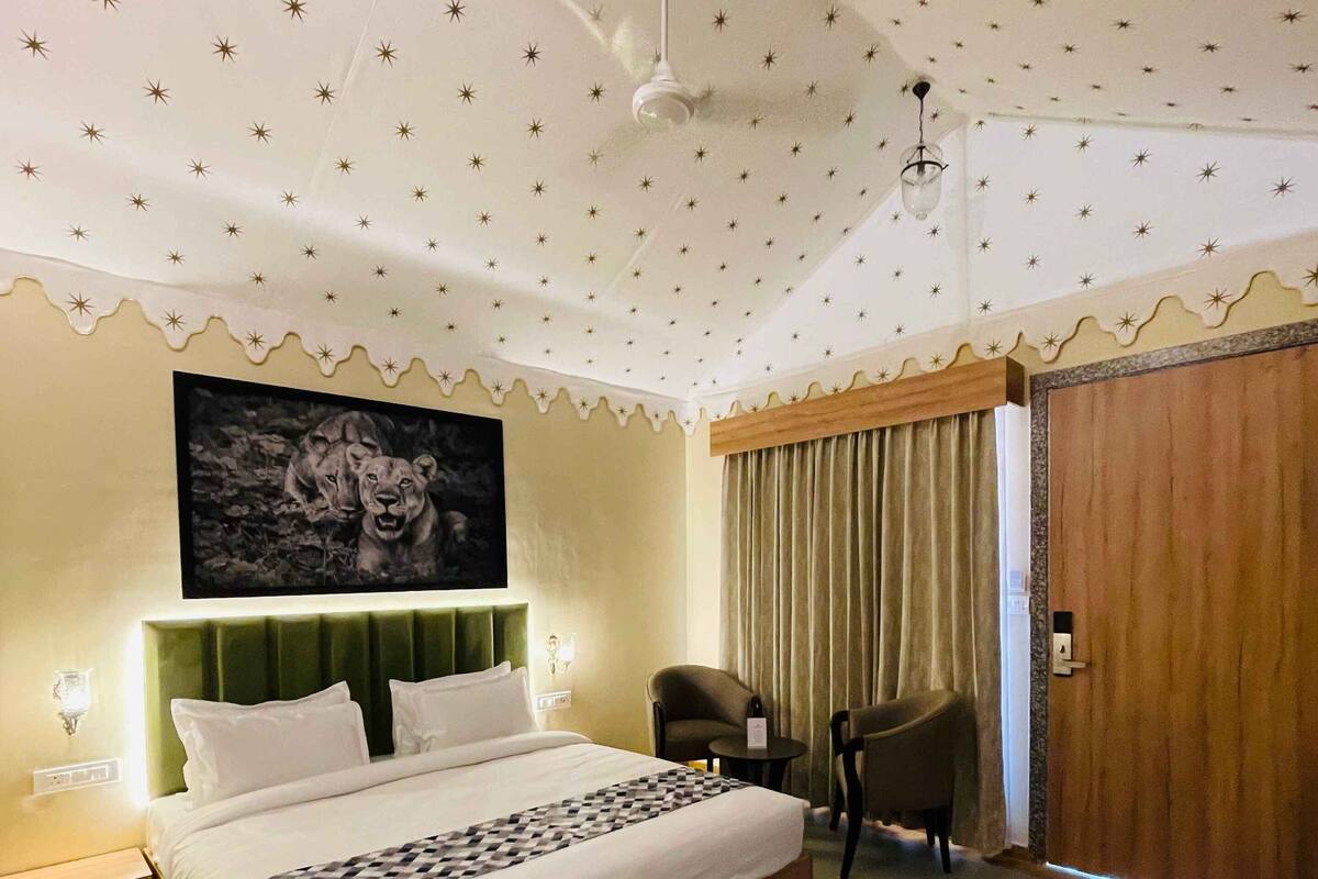 A hotel room with a bed, a chair, a table, a painting, and a ceiling fan.