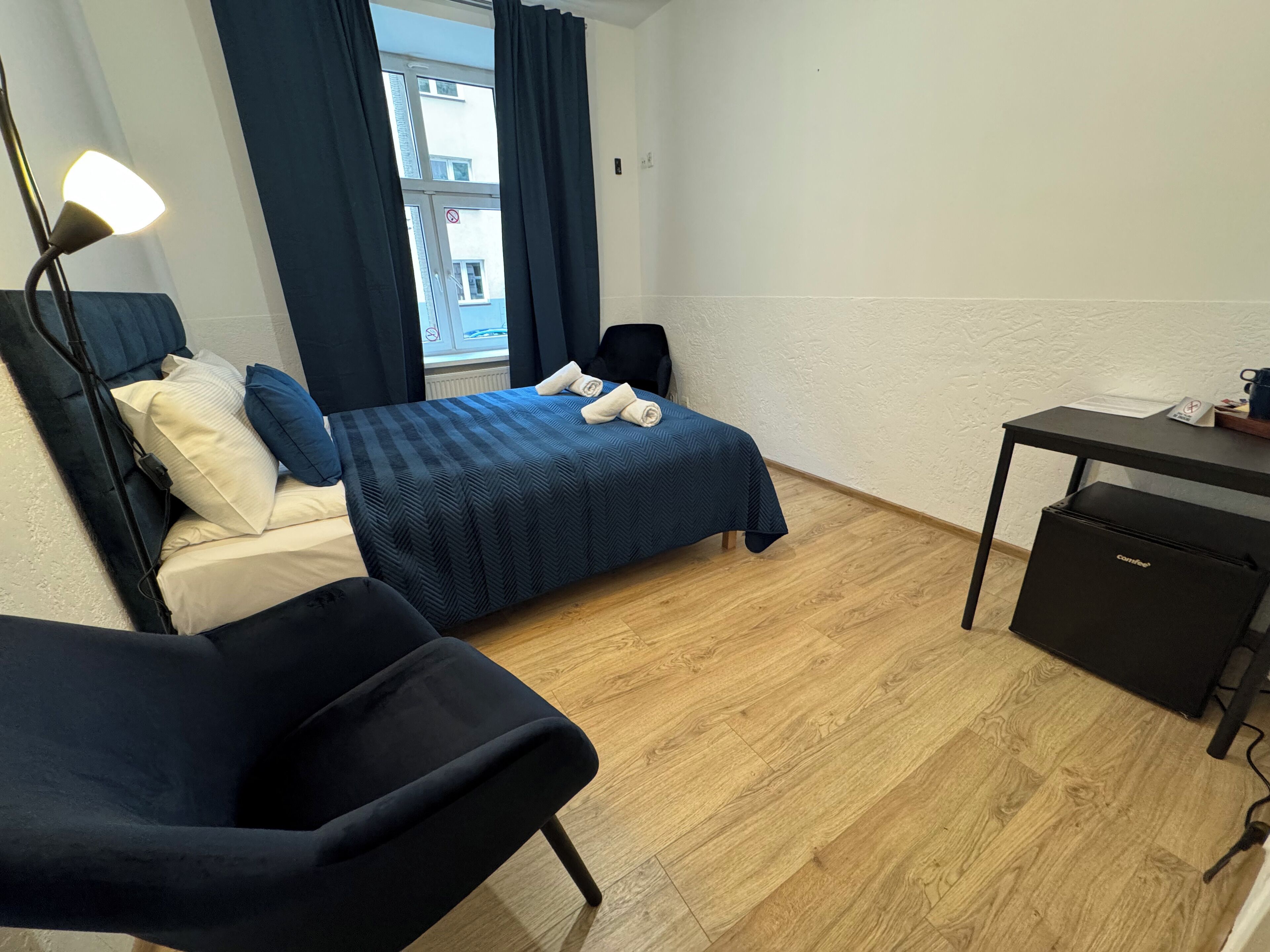 Una camera d'albergo compatta con un letto, una scrivania, una sedia e un piccolo armadietto.