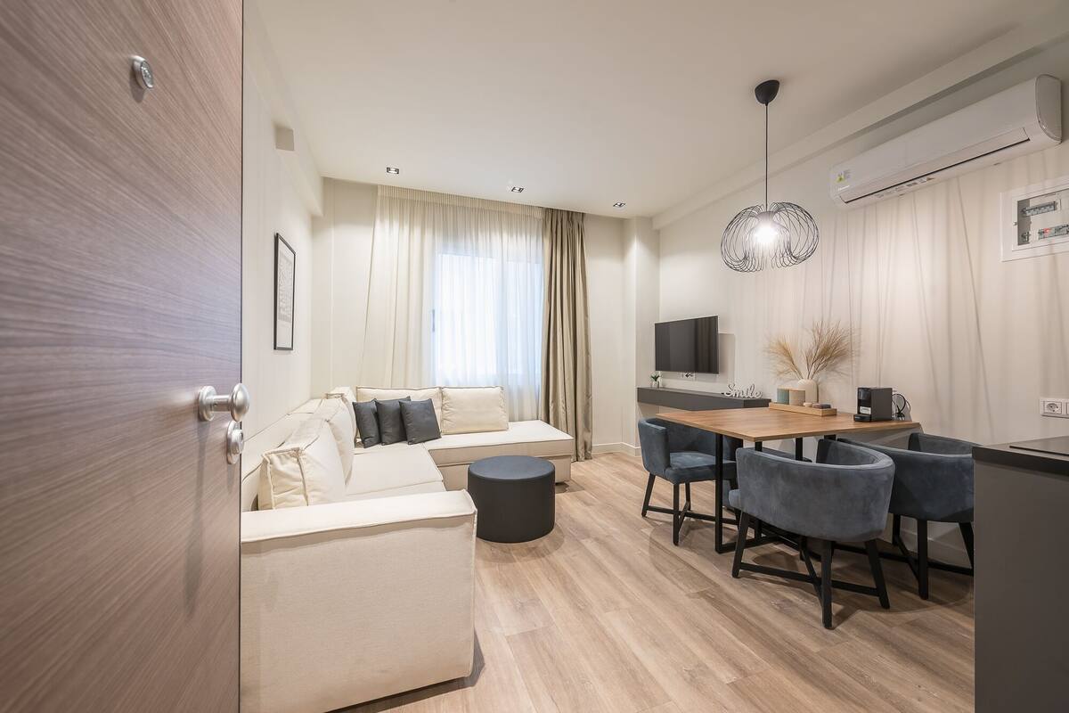 A modern living room with a sofa, a dining table with chairs, a TV, and a hanging light fixture.