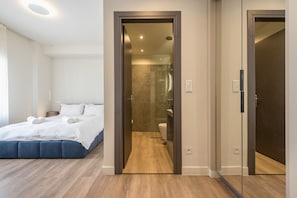 A modern hotel room with a large bed, a walk-in closet, and a separate bathroom with a glass shower enclosure. - Aeiphoria Suites & Rooms - Athens (Athens)