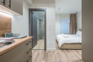 Quarto de hotel moderno com uma escrivaninha de madeira, cama com roupa de cama branca e banheiro visível por uma porta aberta.