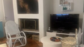 Una sala de estar moderna con un sofá blanco, una cesta de mimbre, una silla blanca, un televisor de pantalla plana y una chimenea.